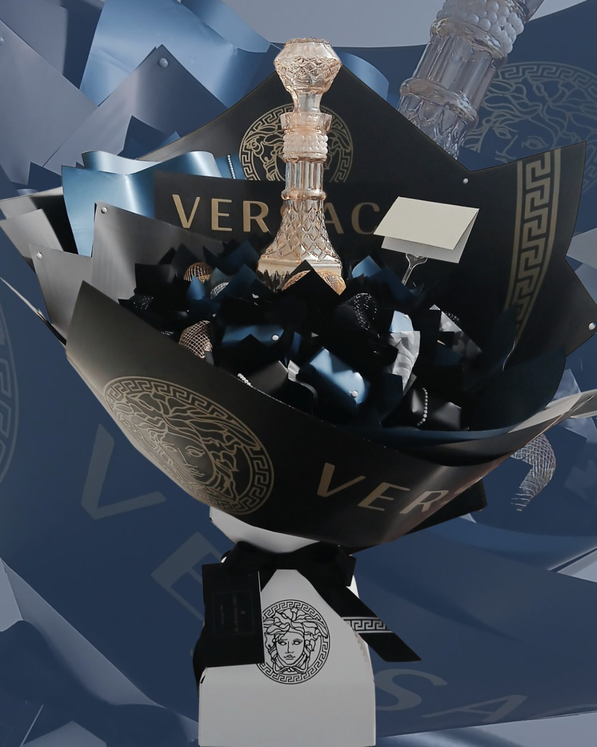 Black and gold designer-style candy bouquet with Versace-themed decorative wrapping; bottle shown for display only